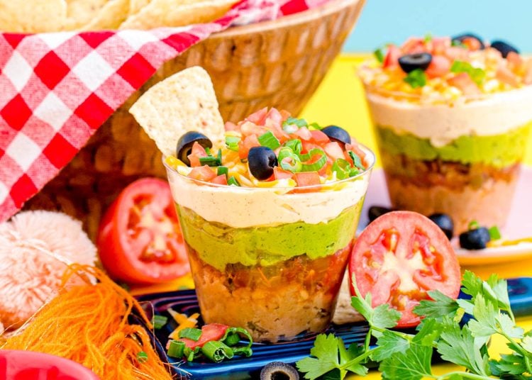7 Layer Dip Cups on a small blue board on a yellow surface.
