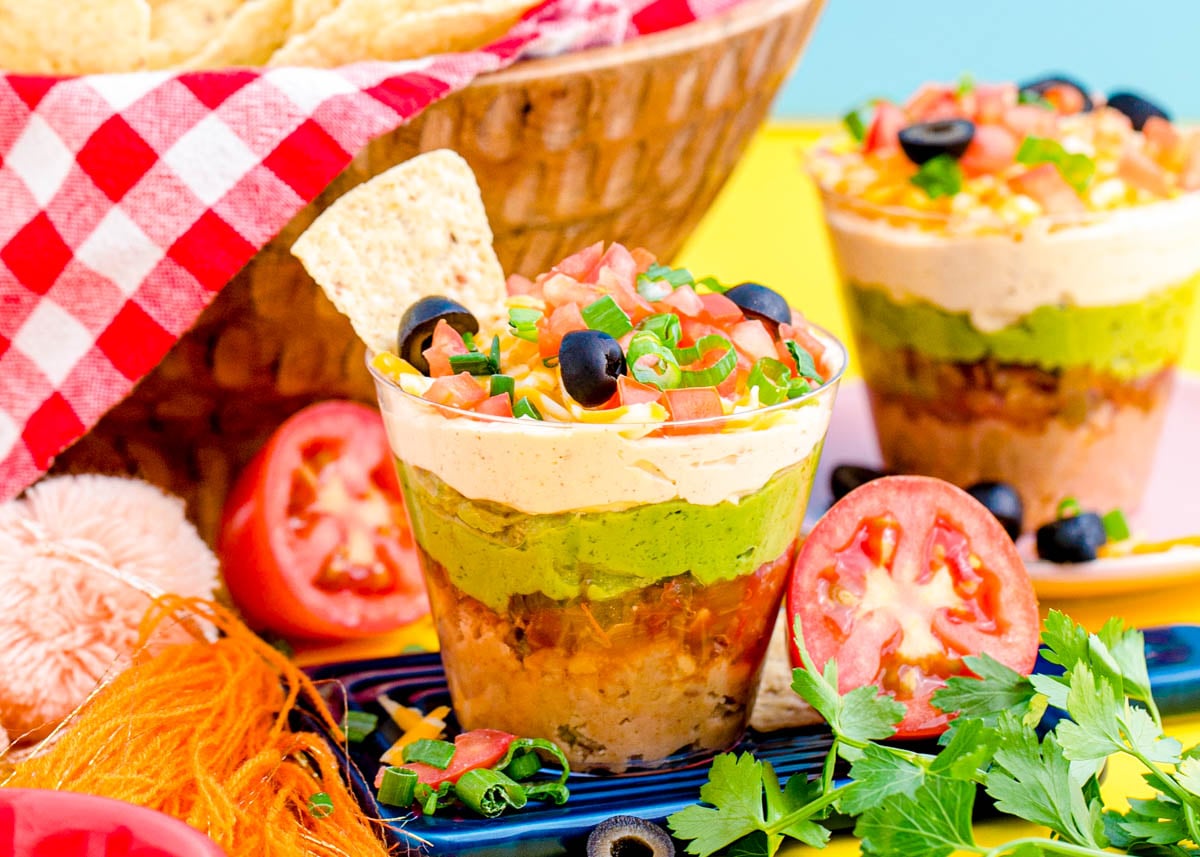 7 Layer Dip Cups on a small blue board on a yellow surface.