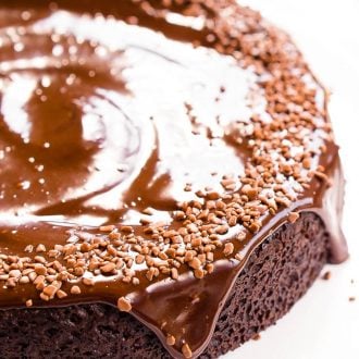 Chocolate Wacky Cake topped with chocolate icing and sprinkles on a white cake stand.