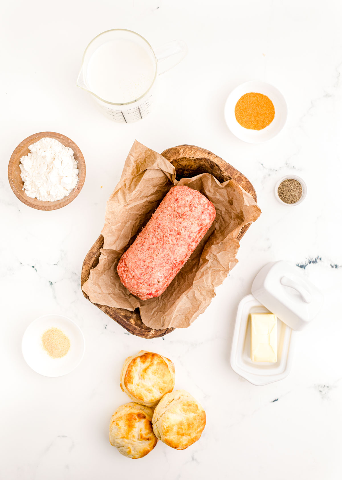 Overhead photo of ingredients to make biscuits and sausage gravy on a white marble counter.