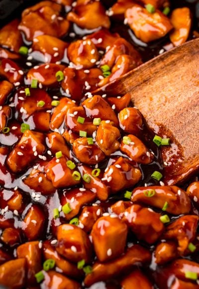 Close up photo of a wooden spatula scooping bourbon chicken out of a pan.