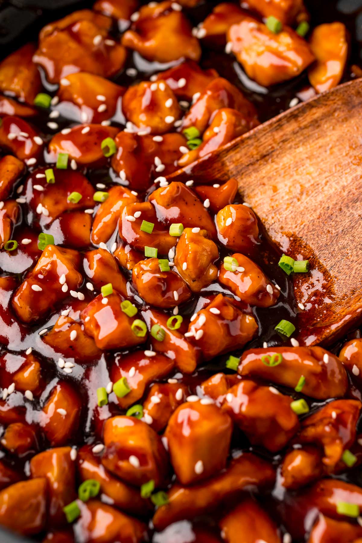 Close up photo of a wooden spatula scooping bourbon chicken out of a pan.