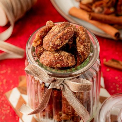Candied Pecans in a glass jar on stacked coasters.