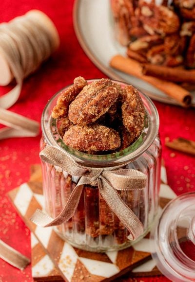 Candied Pecans in a glass jar on stacked coasters.