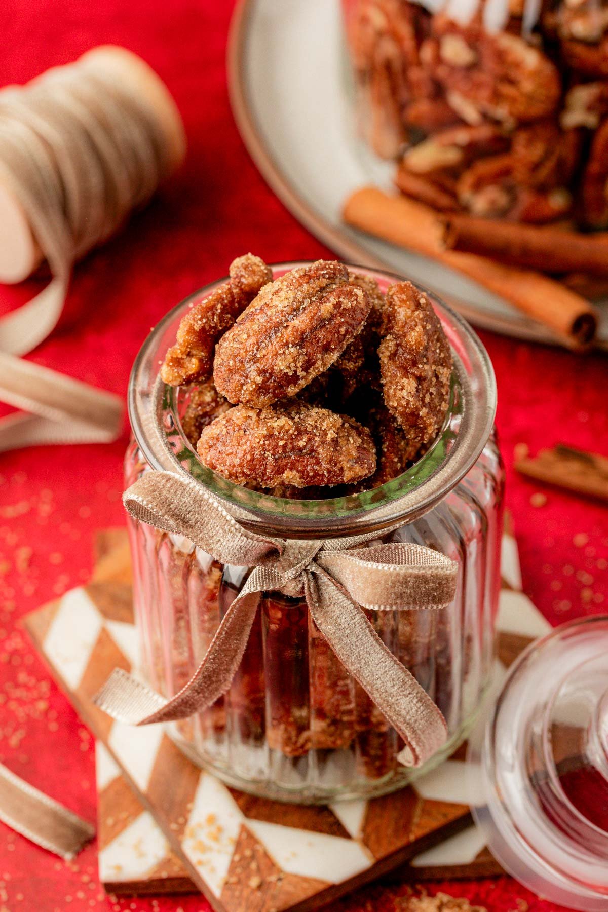 Candied Pecans in a glass jar on stacked coasters. 
