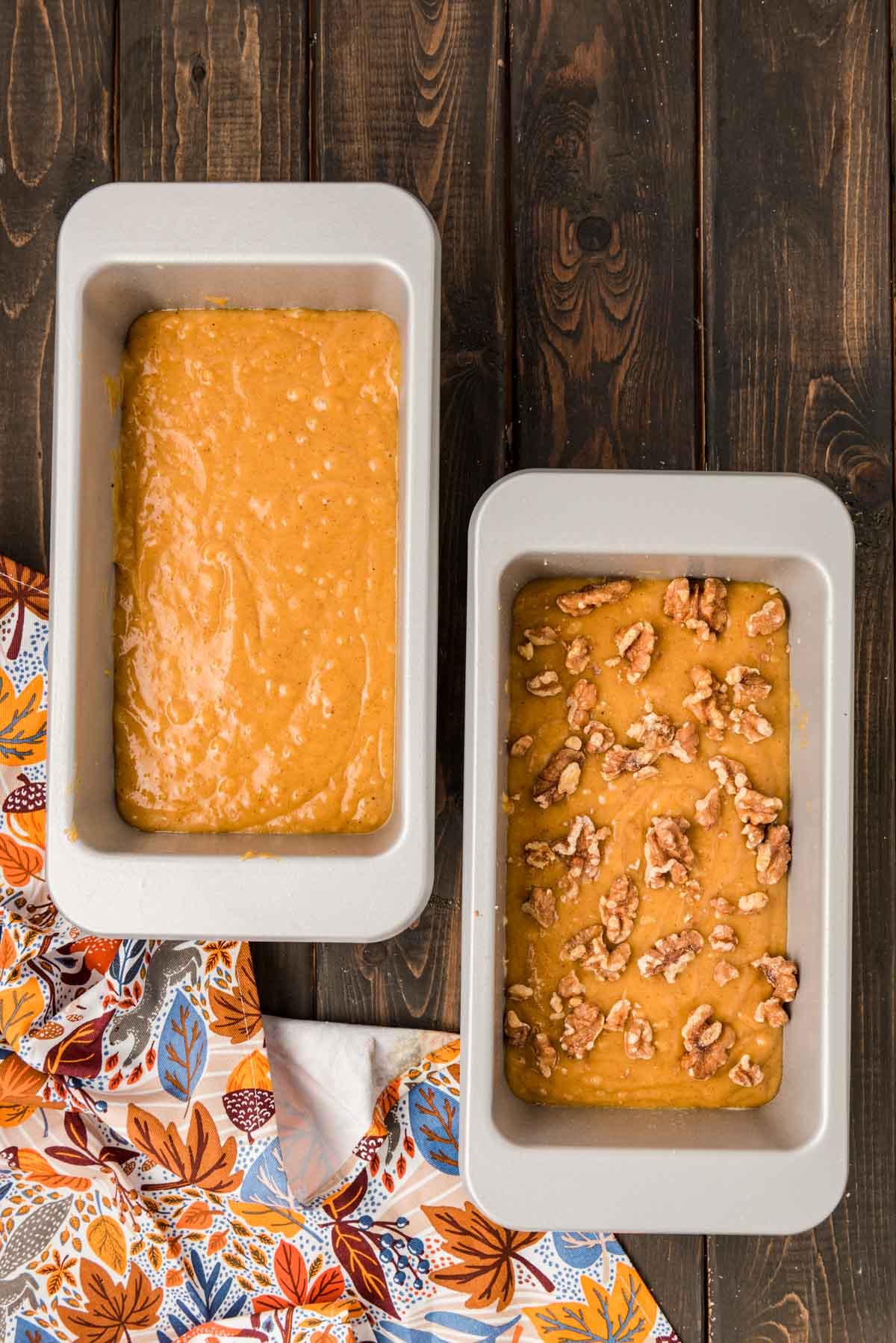 Two loaf pans with pumpkin bread batter in then on a table.