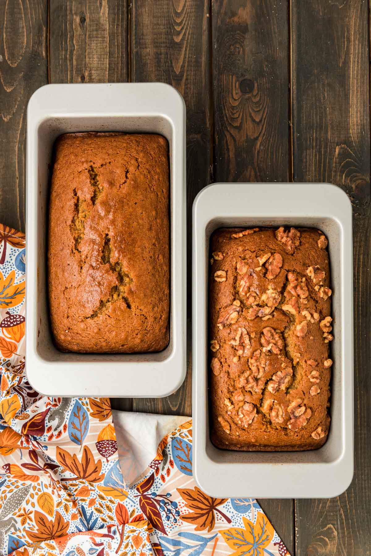 Two loaves of pumpkin bread in pans on a wooden table.