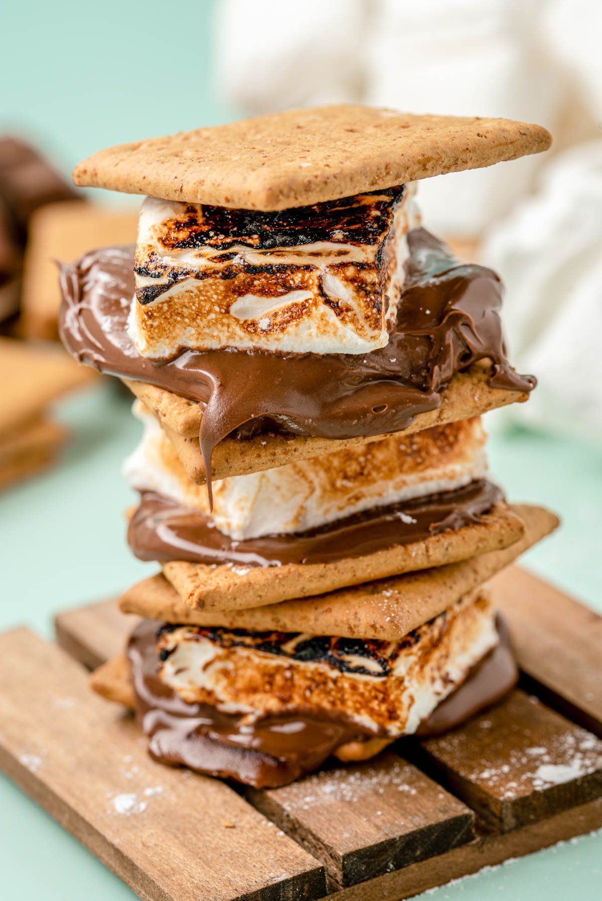 S'mores made with homemade marshmallows stacked on a wooden coaster.