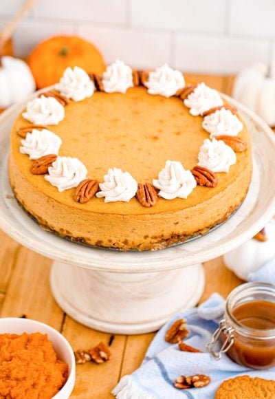 Pumpkin cheesecake on a white cake stand on a wooden table.