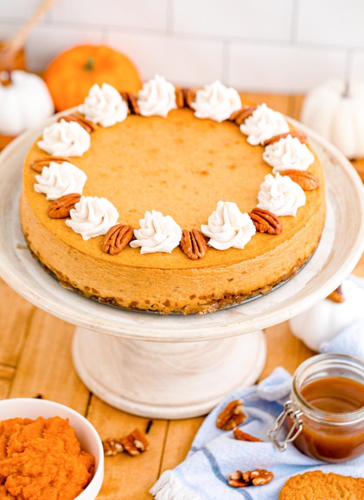 Pumpkin cheesecake on a white cake stand on a wooden table.