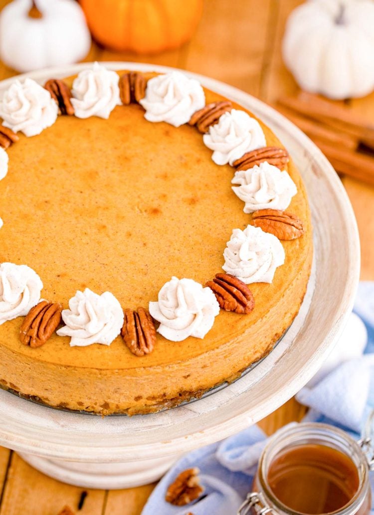 Pumpkin cheesecake on a white cake stand on a wooden table.