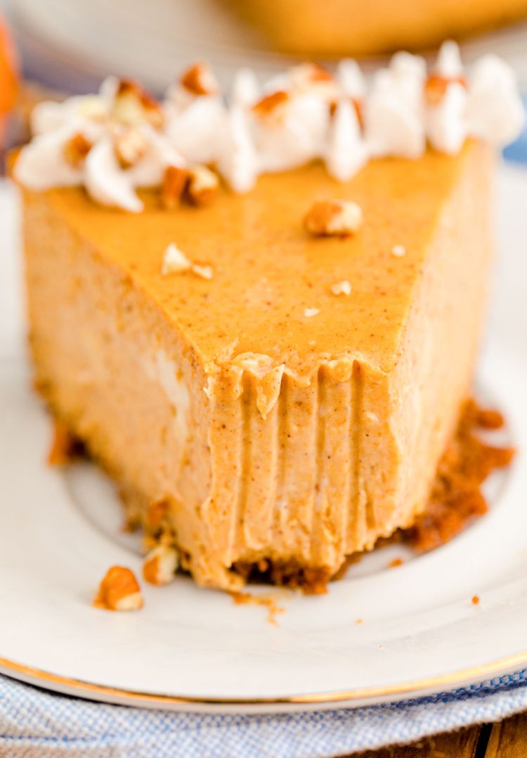 A slice of pumpkin cheesecake on a white plate with a bite taken out if it.