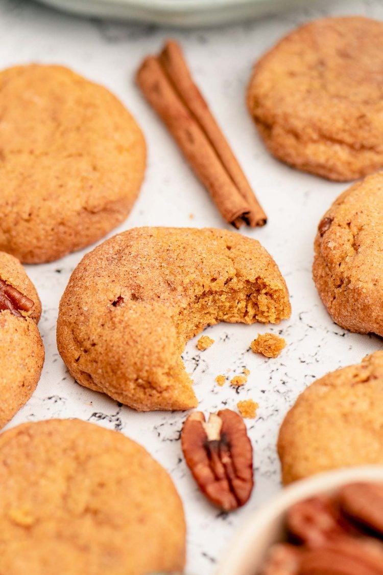 Pumpkin Snickerdoodle cookies on a white counter, one has a bite missing.