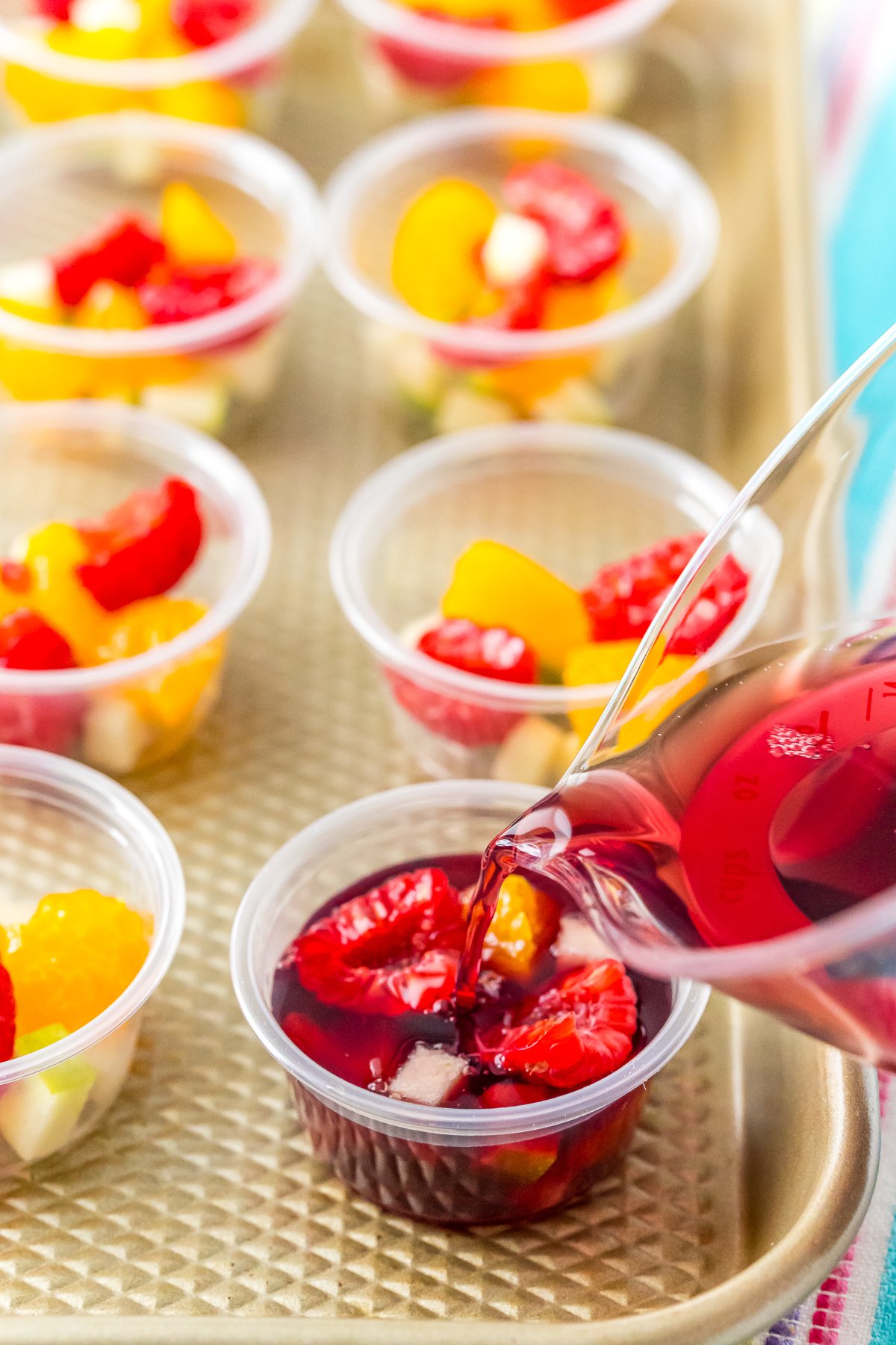 Wine jello mixture being poured into a jello shot cup filled with fruit.