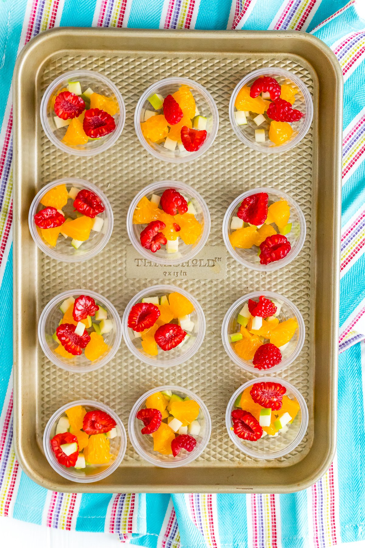 Jello shot cups filled with fruit on a baking sheet.