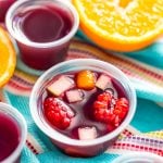 Sangria jello shots on a blue striped napkin with more jello shots and fruit scattered around.
