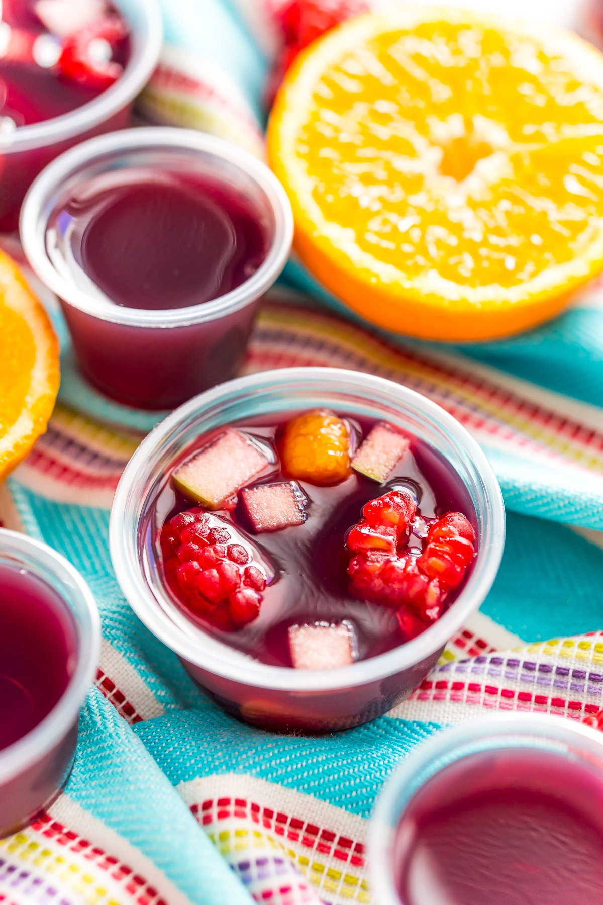 Sangria jello shots on a blue striped napkin with more jello shots and fruit scattered around.