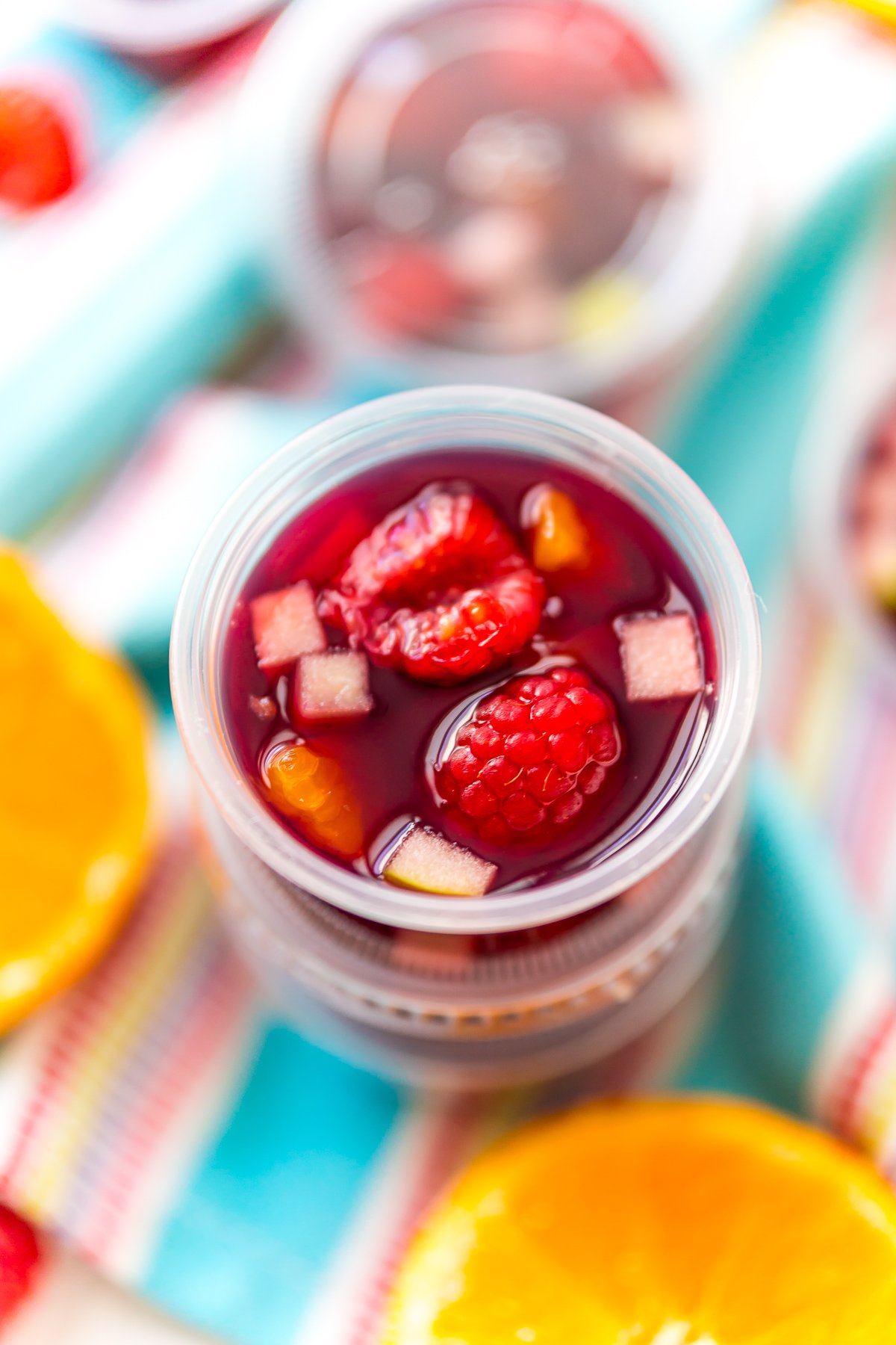 Sangria Jello Shots stacked on top of each other on a blue napkin with fruit scattered around.