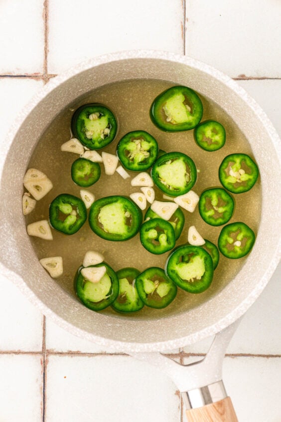 Jalapenos, garlic, vinegar, and more in a saucepan.