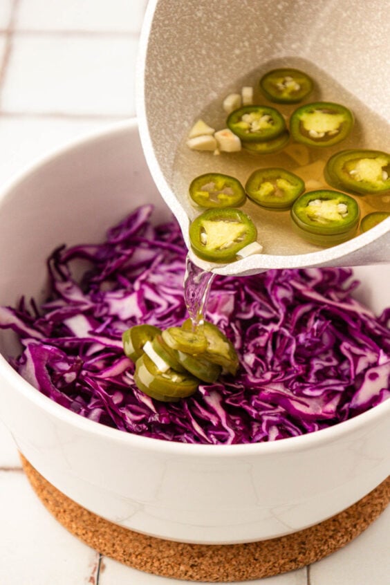 Jalapeno brine being poured over purple cabbage.