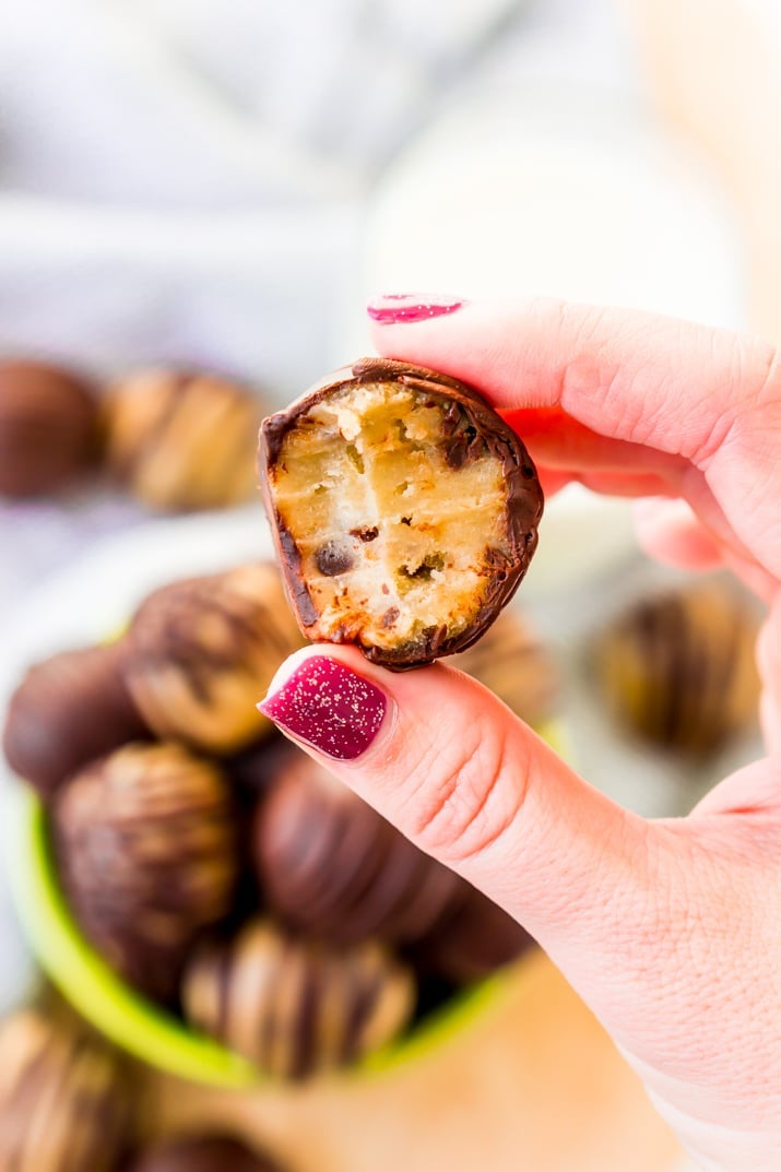 A woman's hand holding a cookie dough truffle that has been bitten into.