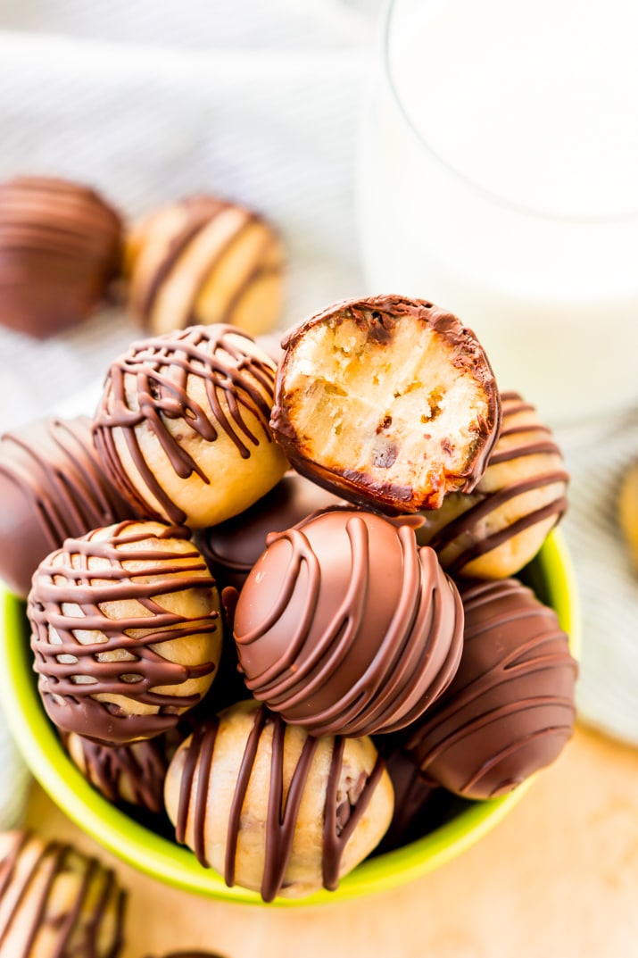 A small green bowl filled with cookie dough truffles. The top truffle has a bite taken off of it.