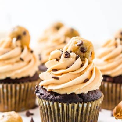 Chocolate cupcakes topped with peanut butter frosting and a mini cookie on a white cake stand.