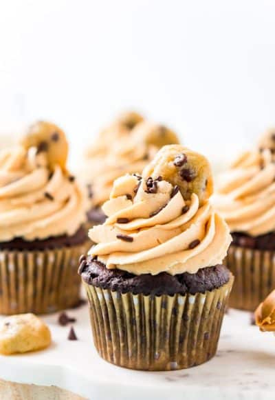 Chocolate cupcakes topped with peanut butter frosting and a mini cookie on a white cake stand.