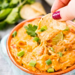 This Slow Cooker Chicken Queso Dip is an easy and addicting party dip made with shredded chicken, cheese, green chiles, tomatoes, green onions, and lots of spice!