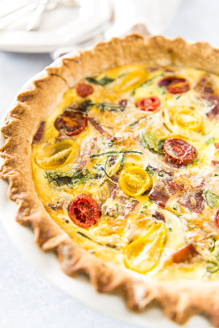 Whole Quiche Lorraine made with bacon, onion, spinach, tomatoes and more in pie dish.