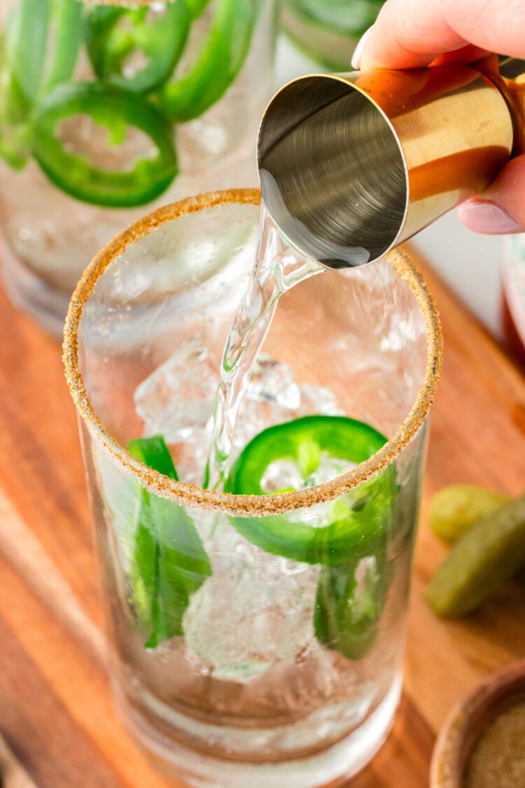 Vodka being poured into glasses with ice and jalapenos.