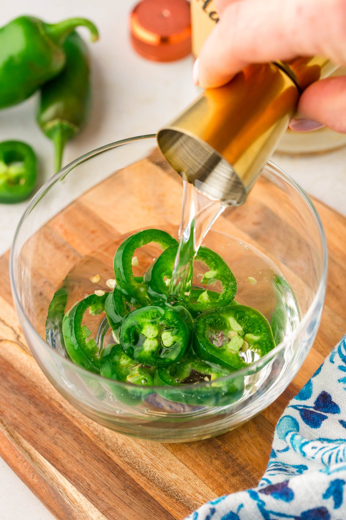 Vodka being poured into a small bowl with sliced jalapenos.