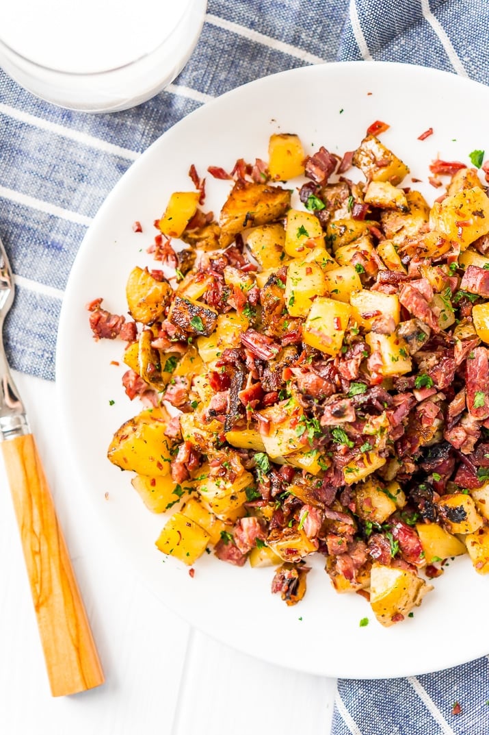 Overhead photo of corned beef hash on white plate with blue napkin