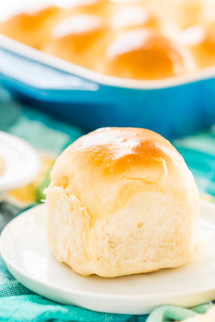 Single yeast roll on small white plate with pan of rolls in background