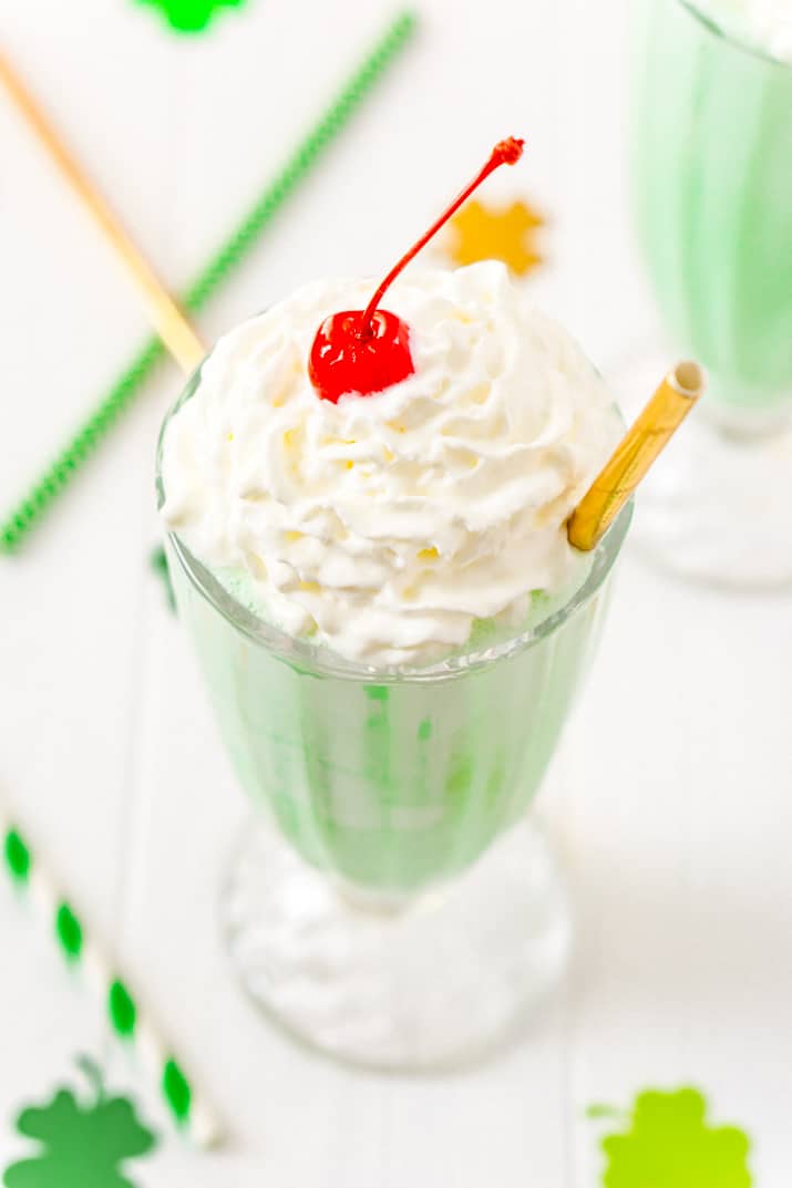 Shamrock Shake Recipe made with vanilla ice cream, milk, mint extract, food coloring, whipped cream, and maraschino cherries.