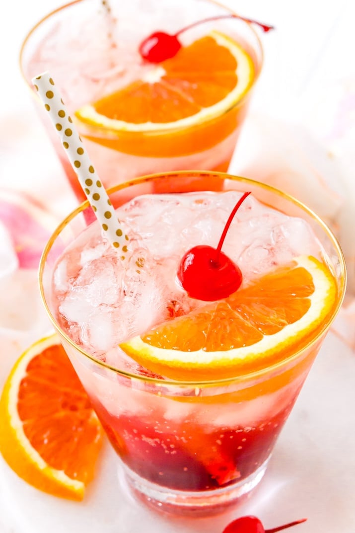 Close up photo of a shirley temple drink garnished with maraschino cherries and orange slices.