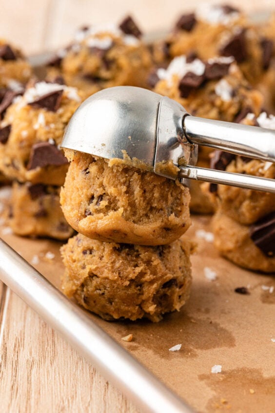 Cookie dough being double stacked with a cookie scoop on a baking pan.