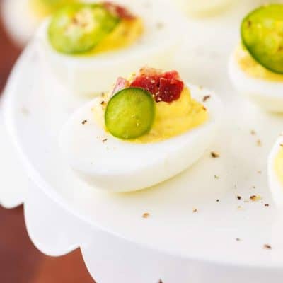Spicy Deviled Eggs are made with mayo, mustard, relish, sriracha, jalapeño, and bacon. This easy recipe is the perfect snack to serve at summertime barbecues and cookouts!