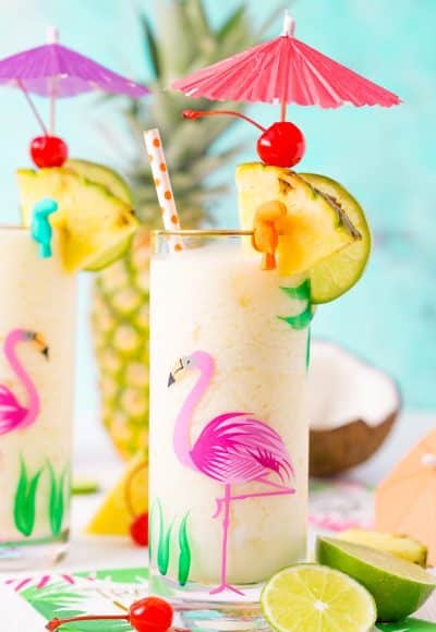 Glass with a flamingo painted on it with a pina colada in it topped with a drink umbrella and pineapple wedge.