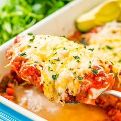 Close up photo of a serving spoon lifting a piece of salsa chicken out of a baking dish.