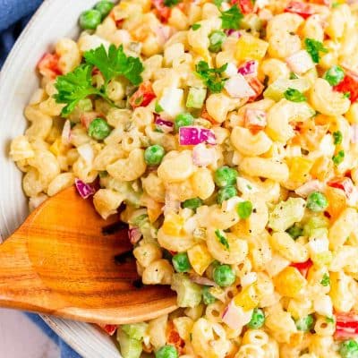 A wooden serving spoon scooping out of a macaroni salad.