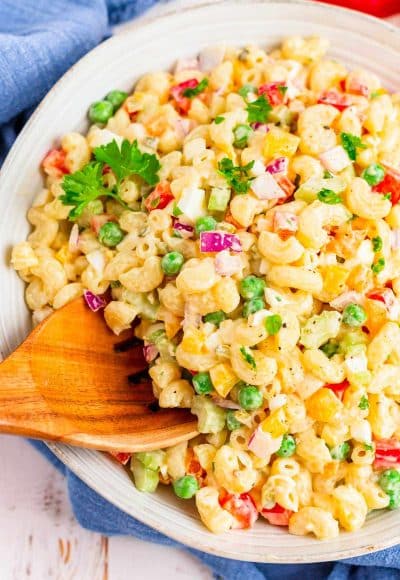 A wooden serving spoon scooping out of a macaroni salad.