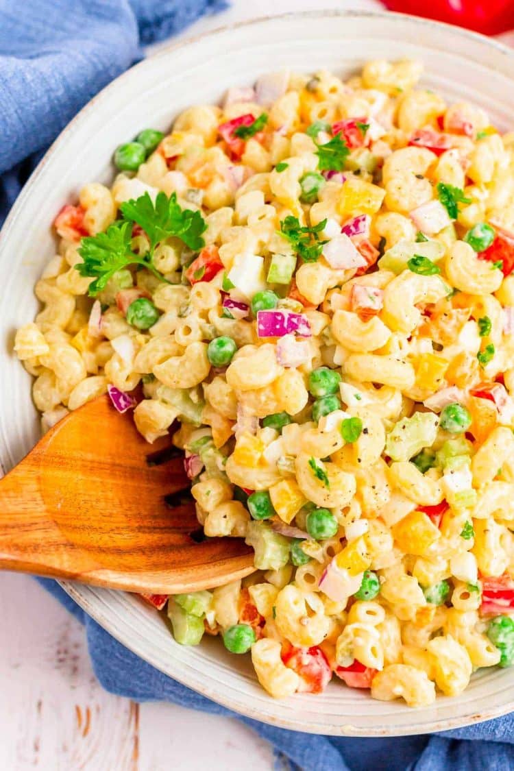 A wooden serving spoon scooping out of a macaroni salad.