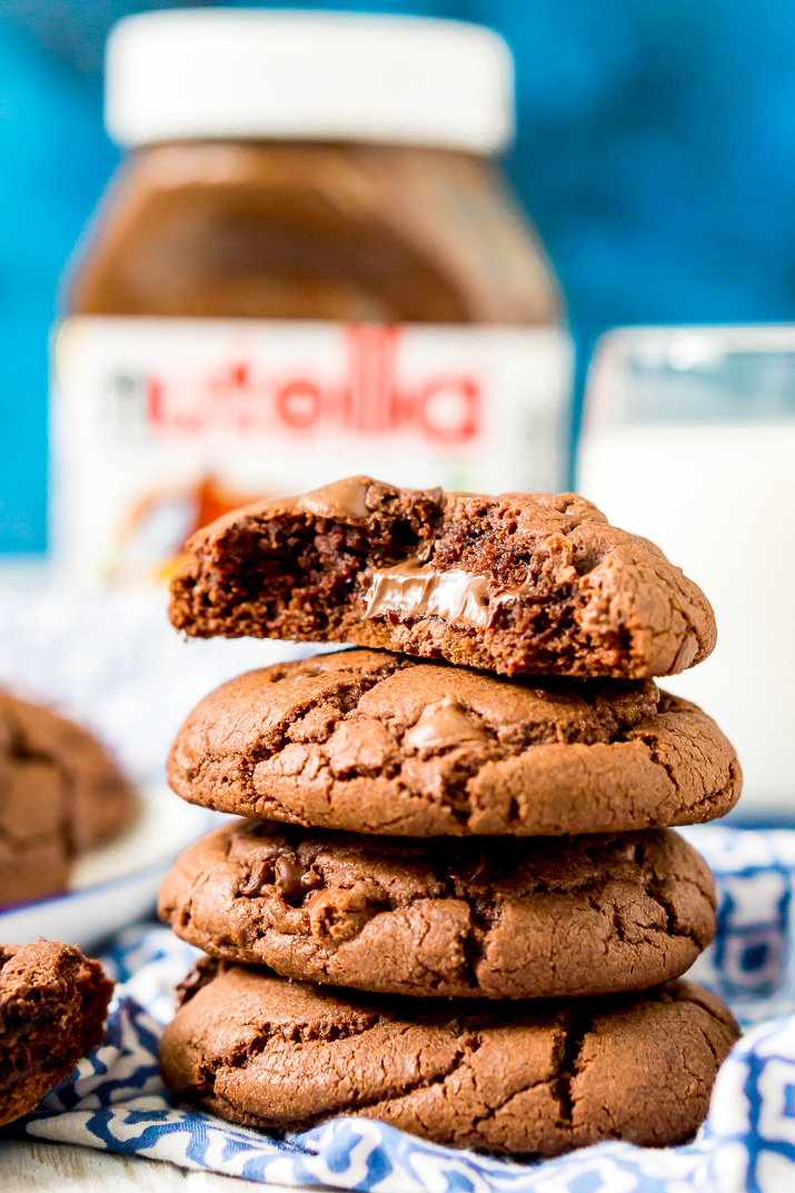 Close up photo of a stack of 4 chocolate cookies on a blue and white napkin, the top one has a bite taken out of it revealing nutella.