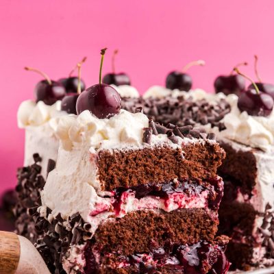 Close up photo of a slice of black forest cake on a cake server being pulled away from the rest of the cake.