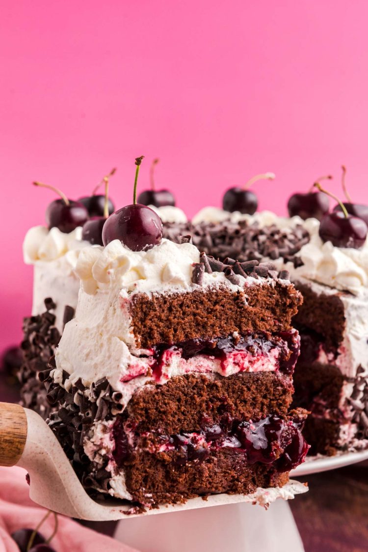 Close up photo of a slice of black forest cake on a cake server being pulled away from the rest of the cake.