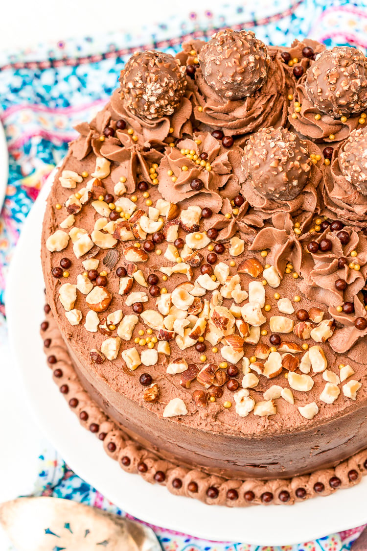 Nutella hazelnut cake on a cake stand topped with Ferrero Rocher candy and chopped hazelnuts.