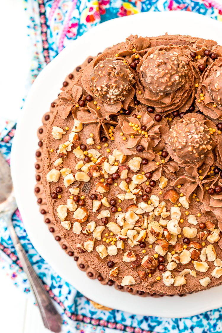 Photo of the top of a chocolate cake topped with chopped hazelnuts and Ferrero Rocher candy.