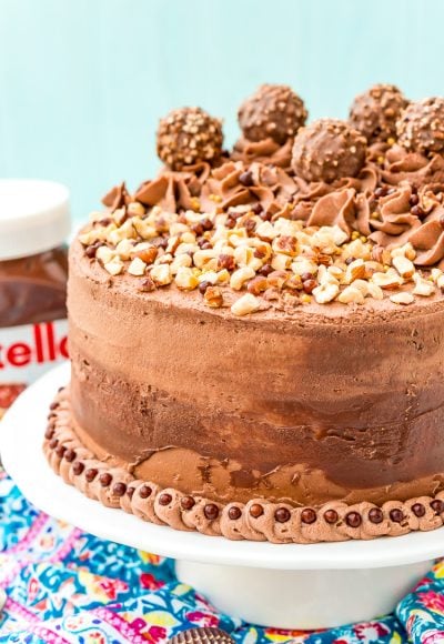 This Nutella Cake is a rich and indulgent dessert highlighting the delicious blend of chocolate and hazelnut! A moist chocolate cake coated in a decadent Nutella frosting and topped with Ferrero Rocher candy and chopped hazelnuts.
