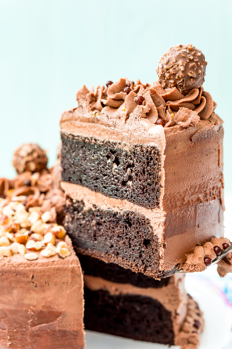 Slice of hazelnut cake being lifted away from the whole cake on a cake stand.